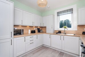 Una cocina moderna con armarios blancos, encimera de madera y ventana con vistas a árboles.