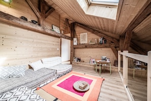 A cozy attic room with a sloped ceiling, wooden beams, a sofa, a small table, and a window. - Holiday Home “Le Chat Perché” with Mountain View and Private Garden (Bernex)