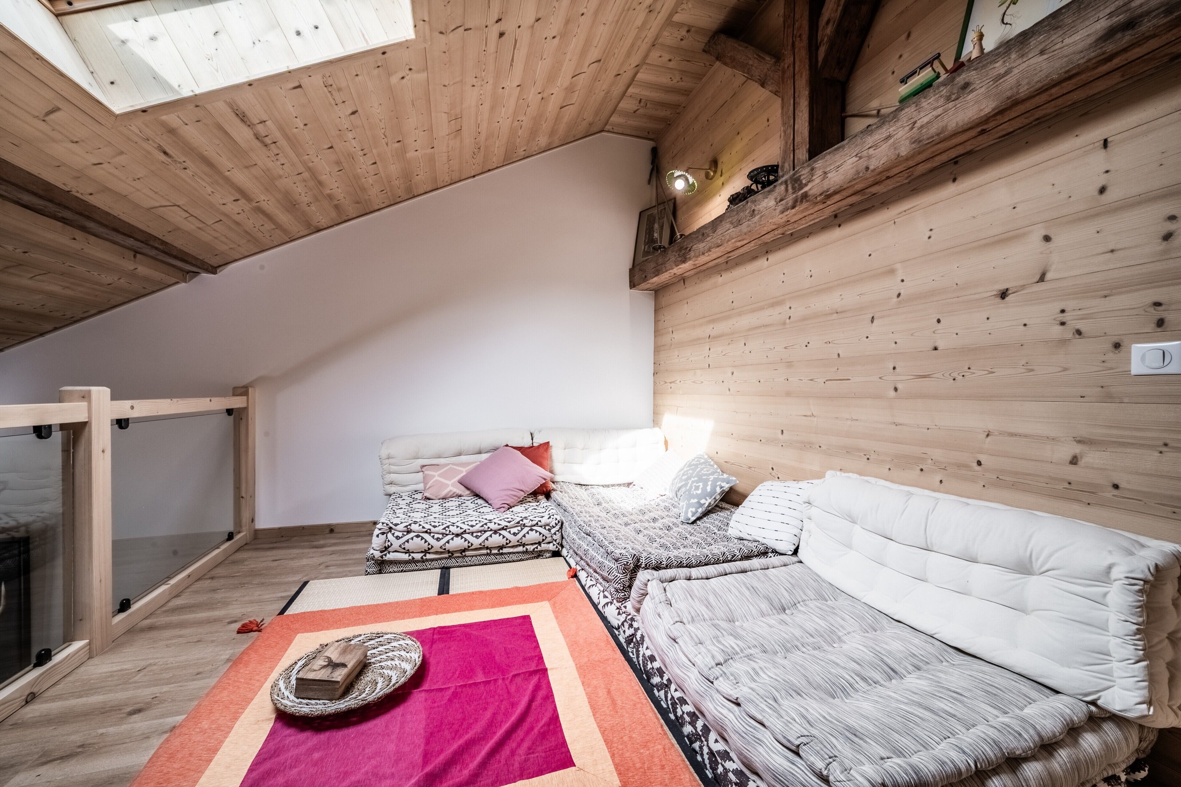Een gezellige kamer met een schuine kap, houten wanden, een bank, een kamerkleed met patroon en een tafeltje met een decoratief object.
