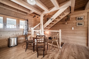 A wooden interior with a dining table, chairs, a staircase, and a trash bin.