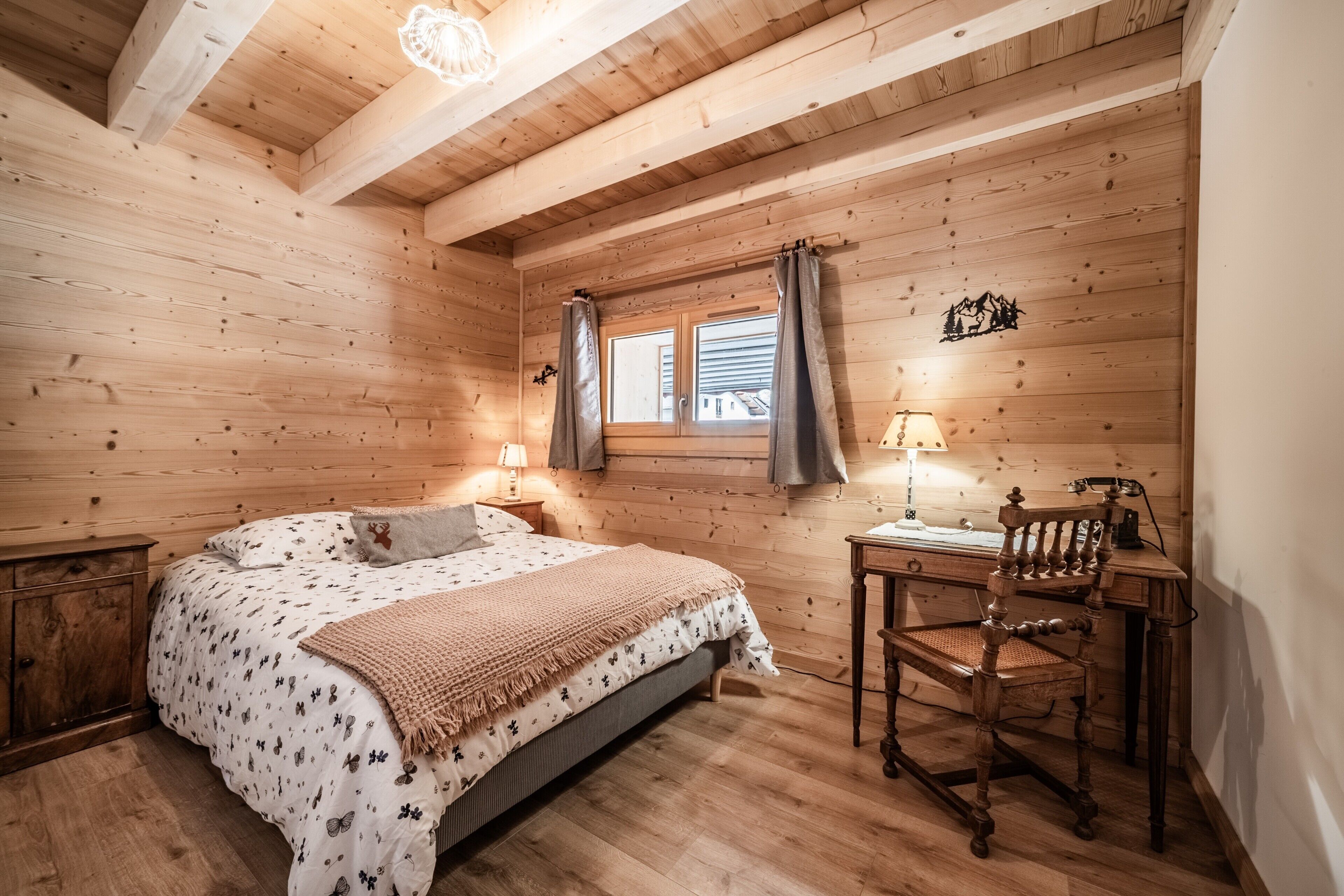 A wooden room with a bed, a desk, and a window with curtains.