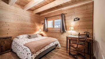 A wooden room with a bed, a desk, and a window with curtains.