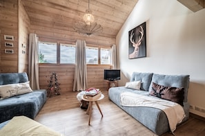 A cozy living room with wooden walls, a large window, a television, and a deer artwork.