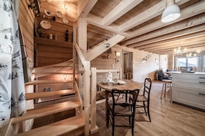 A wooden interior with a staircase, dining table, chairs, and a kitchen area. - Holiday Home “Le Chat Perché” with Mountain View and Private Garden (Bernex)