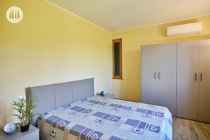 A bedroom with a bed, a nightstand, a potted plant, a wardrobe, and an air conditioning unit. - Tuscan idyll: Apartment near Montecarlo in an olive grove (Toscana)