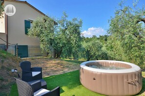 A hot tub in a backyard with a house, green lawn, and trees. - Tuscan idyll: Apartment near Montecarlo in an olive grove (Toscana)