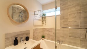 A modern bathroom with a glass-enclosed shower, a round mirror, a sink with two black soap dispensers, and a small potted plant. - 4 Bed House - Cheltenham & Gloucester - Sleeps 8 (Gloucester)