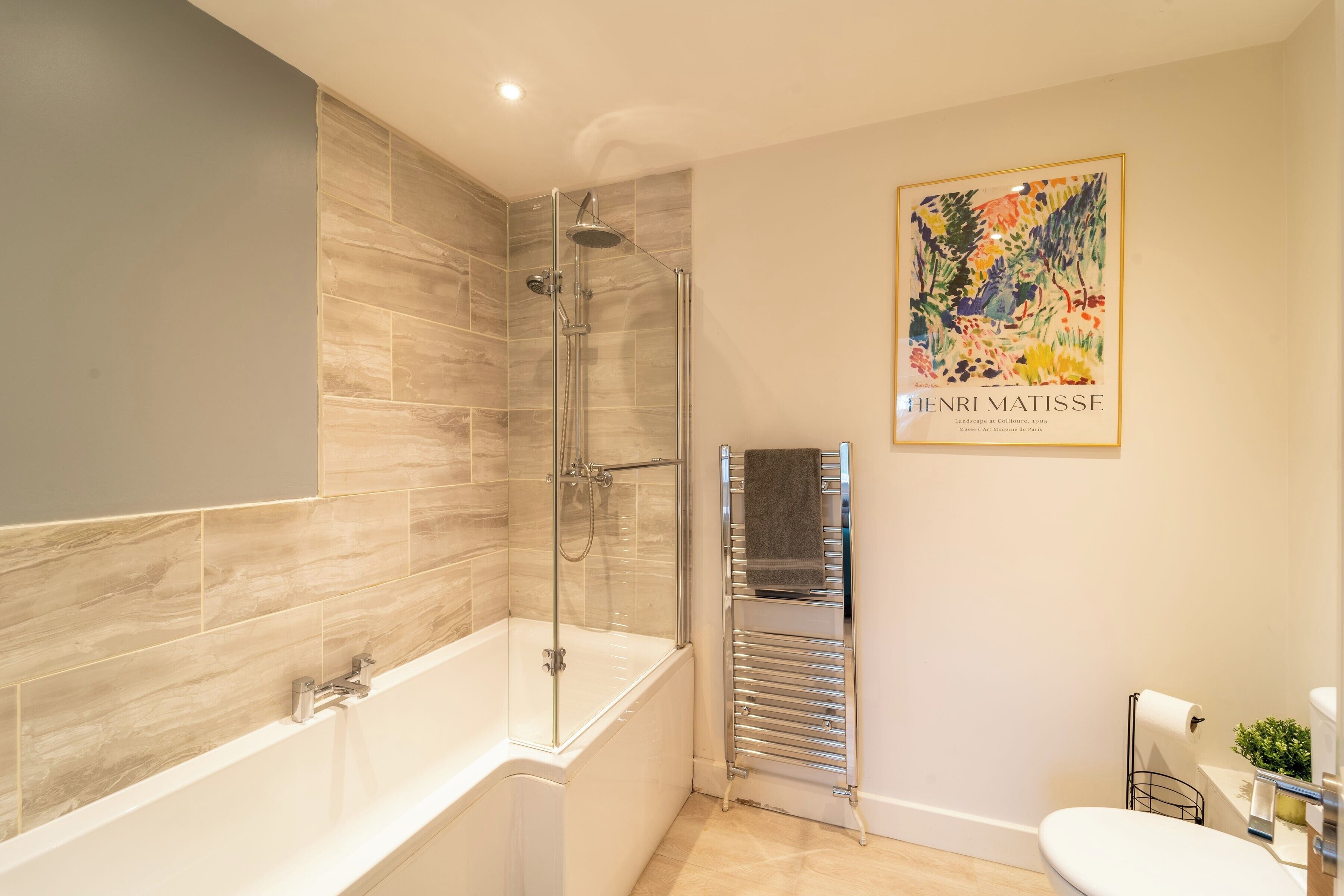 A modern bathroom with a glass-enclosed shower, a white bathtub, and a toilet.