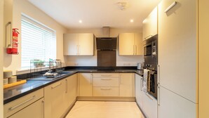 A modern kitchen with light-colored cabinets, a black countertop, stainless steel appliances, and a fire extinguisher on the wall. - 4 Bed House - Cheltenham & Gloucester - Sleeps 8 (Gloucester)