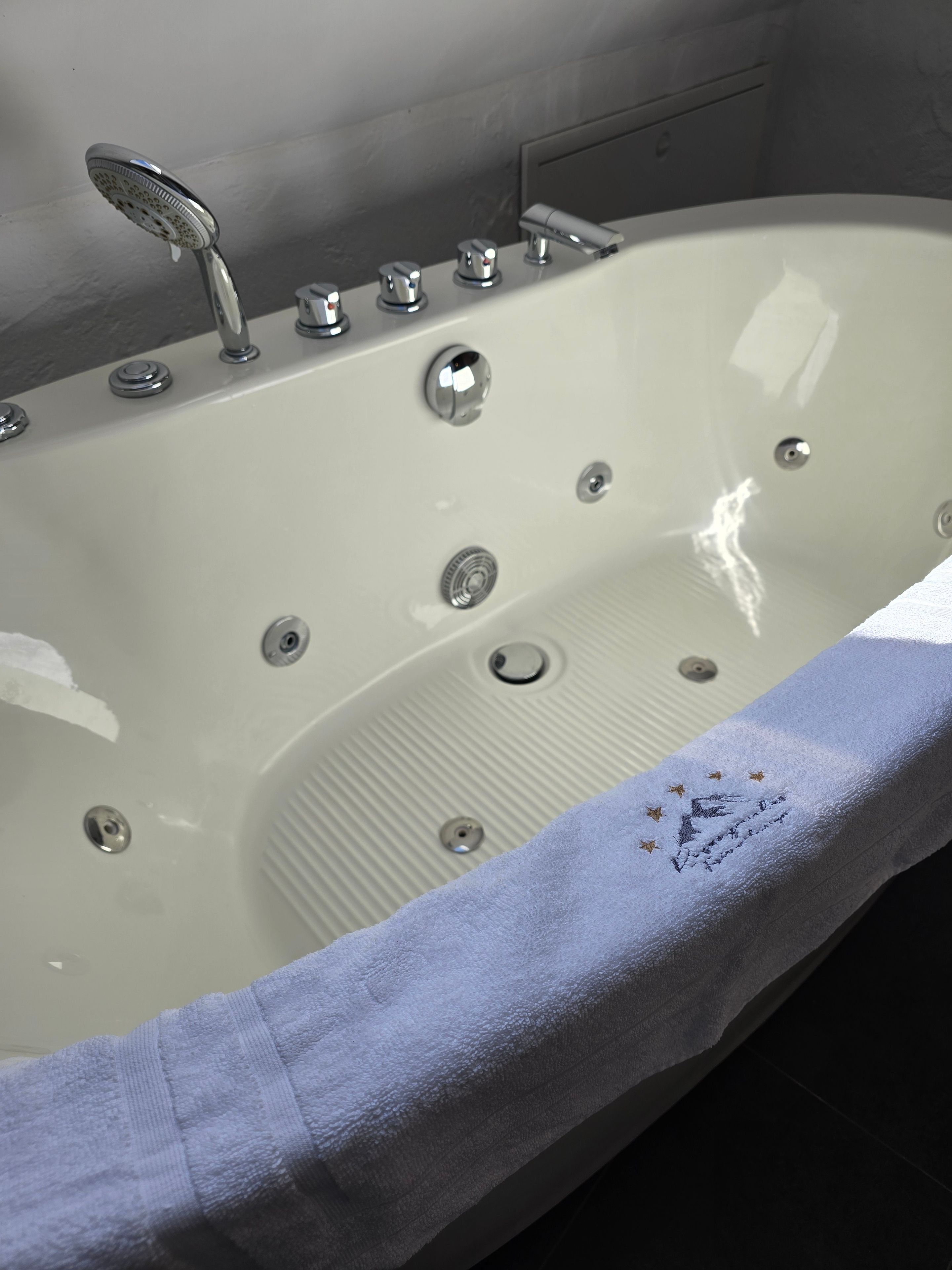 Eine Badewanne mit mehreren Wasserhähnen und einem Abfluss, ein Handtuch mit Sternenmuster und ein gefliester Boden.