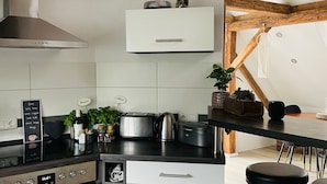 A kitchen with a built-in oven, a stainless steel range hood, a white cabinet, and a wooden ceiling.