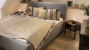 A bedroom with a sloped ceiling, a bed with a grey headboard, bedside tables with lamps, and a small wooden nightstand.