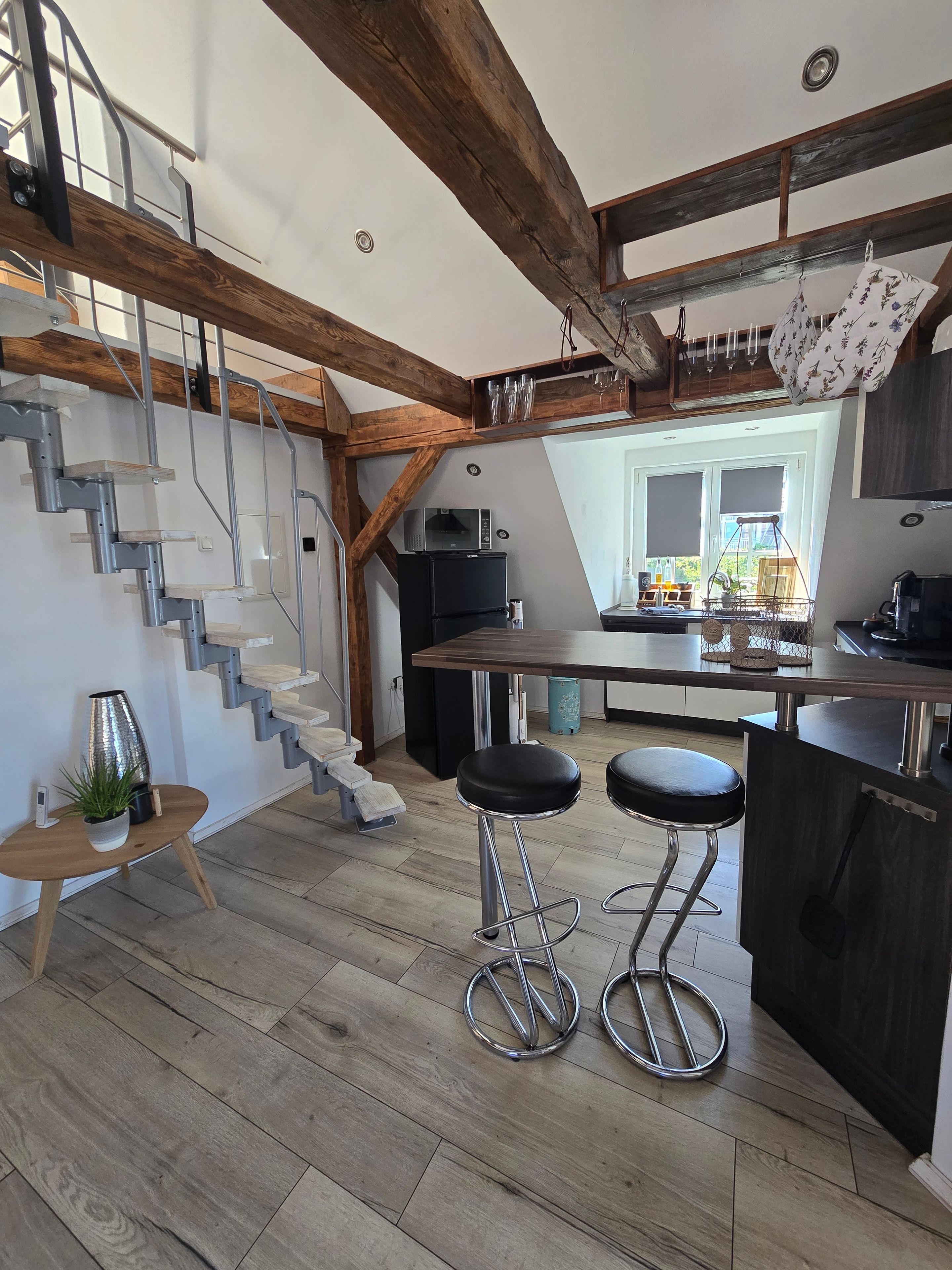 Een moderne keuken met een houten trap, een eethoek met krukken en uitzicht op de omgeving.