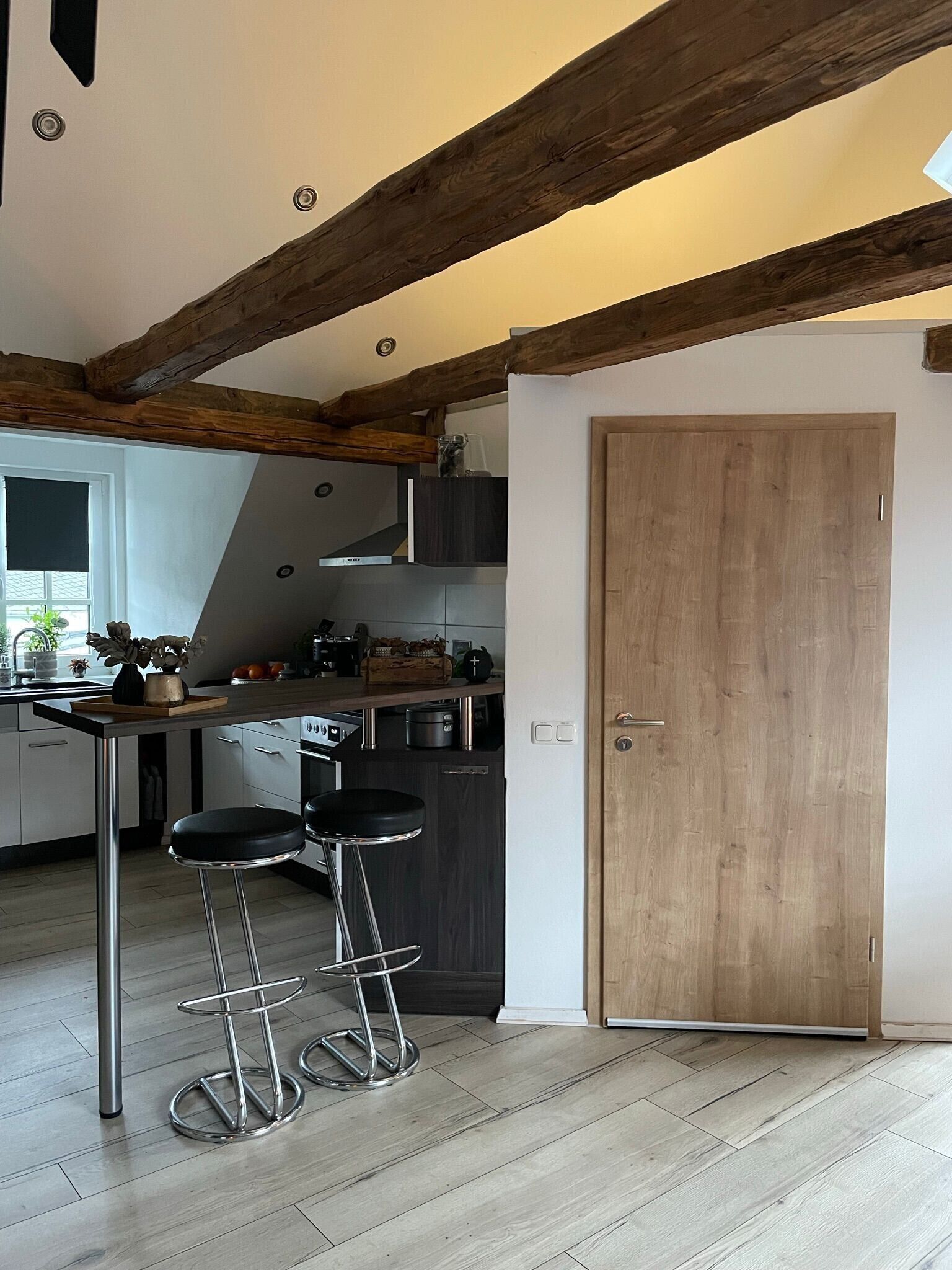 A kitchen with wooden beams, a stove, bar stools, and a door.