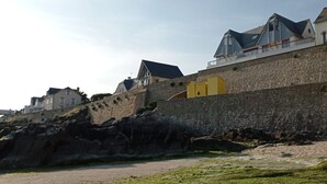 Ein Küstengebäude mit Steinmauer, gelber Tür und steilem, felsigen Gelände.