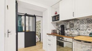 Eine kleine Küche mit weißen Schränken, einer Holz Arbeitsplatte, einer Mikrowelle und einer ornamental gestalteten Spritzschutzleiste.