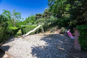 A playground with a slide and climbing structure surrounded by greenery.