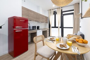 Cuina petita amb un frigorífic vermell, armaris de fusta, una taula de dinar amb articles per esmorzar i una vista per una finestra gran.