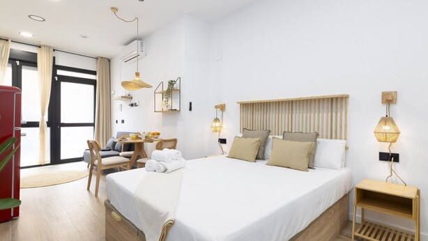 A modern hotel room with a large bed, a desk with a chair, a red refrigerator, and a large window with curtains. - Travel Habitat Nou Mestalla 2 (Valencia)
