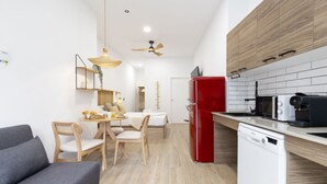 A modern kitchen with a red refrigerator, white dishwasher, and wooden cabinets. There is a dining area with a table and chairs, and a gray sofa in the foreground. - Travel Habitat Nou Mestalla 2 (Valencia)