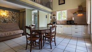 Un coin repas comprenant une table ronde, quatre chaises, un canapé et une cuisine avec des meubles blancs et un fourneau.