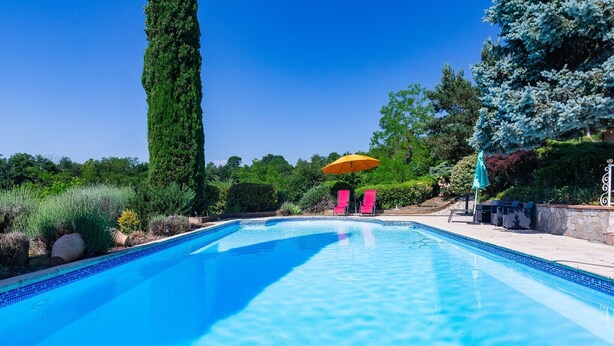 Une piscine dont le bord est recouvert de carrelage, entourée de verdure et surplombée d’un ciel dégagé.