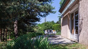 Une maison avec un patio, une table et des chaises, et un jardin avec des arbres et des plantes.