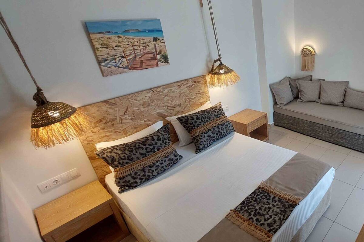 A bedroom with a bed, bedside tables, a nightstand, a sofa, and a wall-mounted lamp.