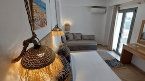 A bedroom with a bed, a sofa, a wooden dresser, a TV, and a hanging lamp. - Selinopetra Rooms (Elafonisos)