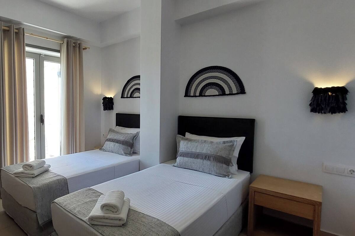 A hotel room with two beds, a desk, a TV, and a window with curtains.