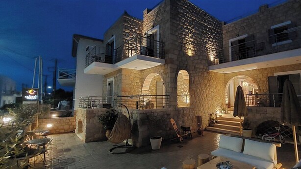 A stone building with arched doorways and a balcony, featuring outdoor seating and a staircase leading to the upper level. - Selinopetra Rooms (Elafonisos)