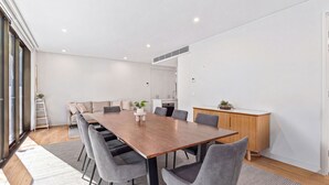 A modern meeting room with a wooden table, grey chairs, a whiteboard, and a kitchenette in the background. - 250SQM Cosy Bondi Escape Luxe 3BR & Parking (Bondi Beach)