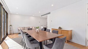 Uma sala de reuniões moderna com mesa de madeira, cadeiras cinzas, um quadro branco e uma pequena cozinha ao fundo.