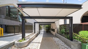 A covered walkway with a fire exit sign, a gated entrance, and a pathway lined with gravel and plants. - 250SQM Cosy Bondi Escape Luxe 3BR & Parking (Bondi Beach)