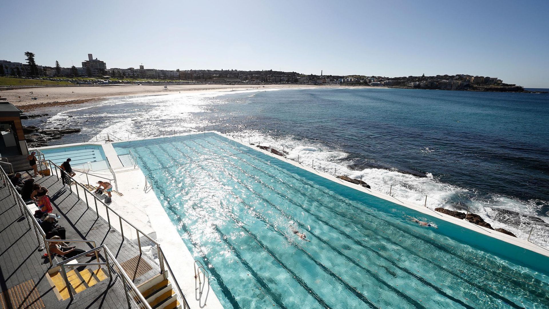A swimming pool adjacent to a beach with waves crashing onto the shore.