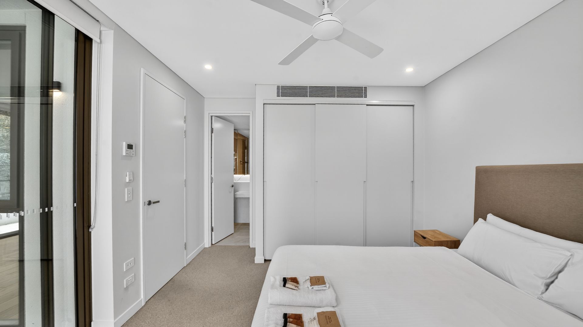 A modern hotel room with a large bed, a ceiling fan, a walk-in closet, and a bathroom visible through an open door.