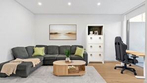 A modern living room with a sectional sofa, a coffee table, and a desk with a chair. - 250SQM Cosy Bondi Escape Luxe 3BR & Parking (Bondi Beach)