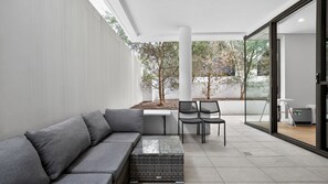 Un espace extérieur moderne, aménagé avec un canapé gris, une petite table et deux chaises.