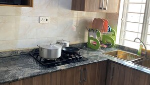 A kitchen with wooden cabinets, a gas stove, pots, a frying pan, a sink, and a window. - Simple And Classic With Affordable Family Bliss At DT-HOMES (ibadan)