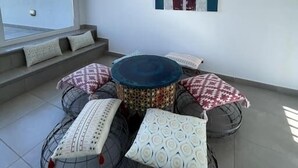 A balcony with a round table and multiple patterned cushions, a view of buildings, and a framed artwork on the wall. - Stylish 1BR City Apartment with Stunning Rooftop Terrace (Gibraltar)