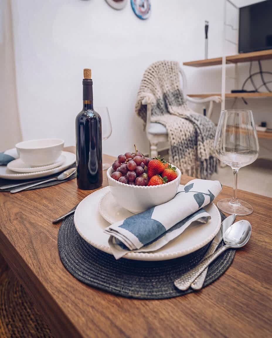 A dining table set with plates, a bowl of fruit, a wine bottle, and a glass.