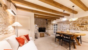 A modern living room with a sofa, dining table, and chairs. There is a fireplace, a TV, and a stone wall. - Casa di Pietra Stone House (Kaštel Lukšić)