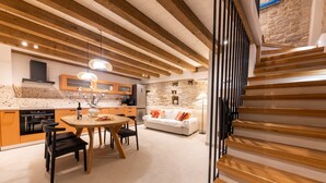 A modern kitchen with wooden beams, a dining area with a round table, and a stone wall in the background. - Casa di Pietra Stone House (Kaštel Lukšić)