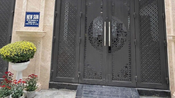 Entrada de un edificio con puertas decorativas grandes, un cartel y plantas en macetas.