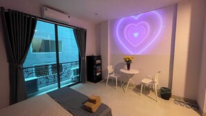 Habitación de hotel con cama, una pequeña mesa con sillas, un elemento decorativo proyectado en la pared y un balcón con vistas.