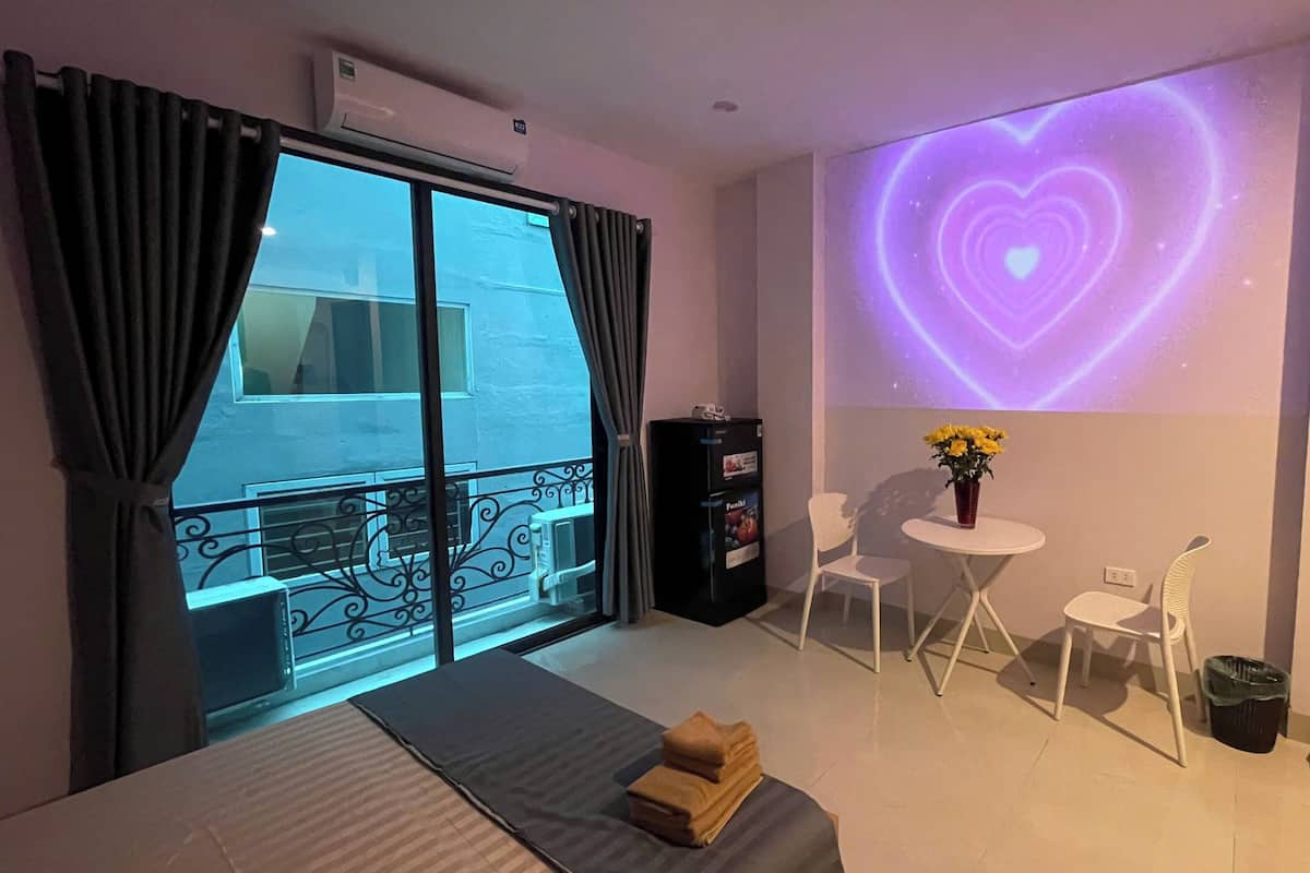 A hotel room with a bed, a small table with chairs, a decorative wall projection, and a balcony with a view.