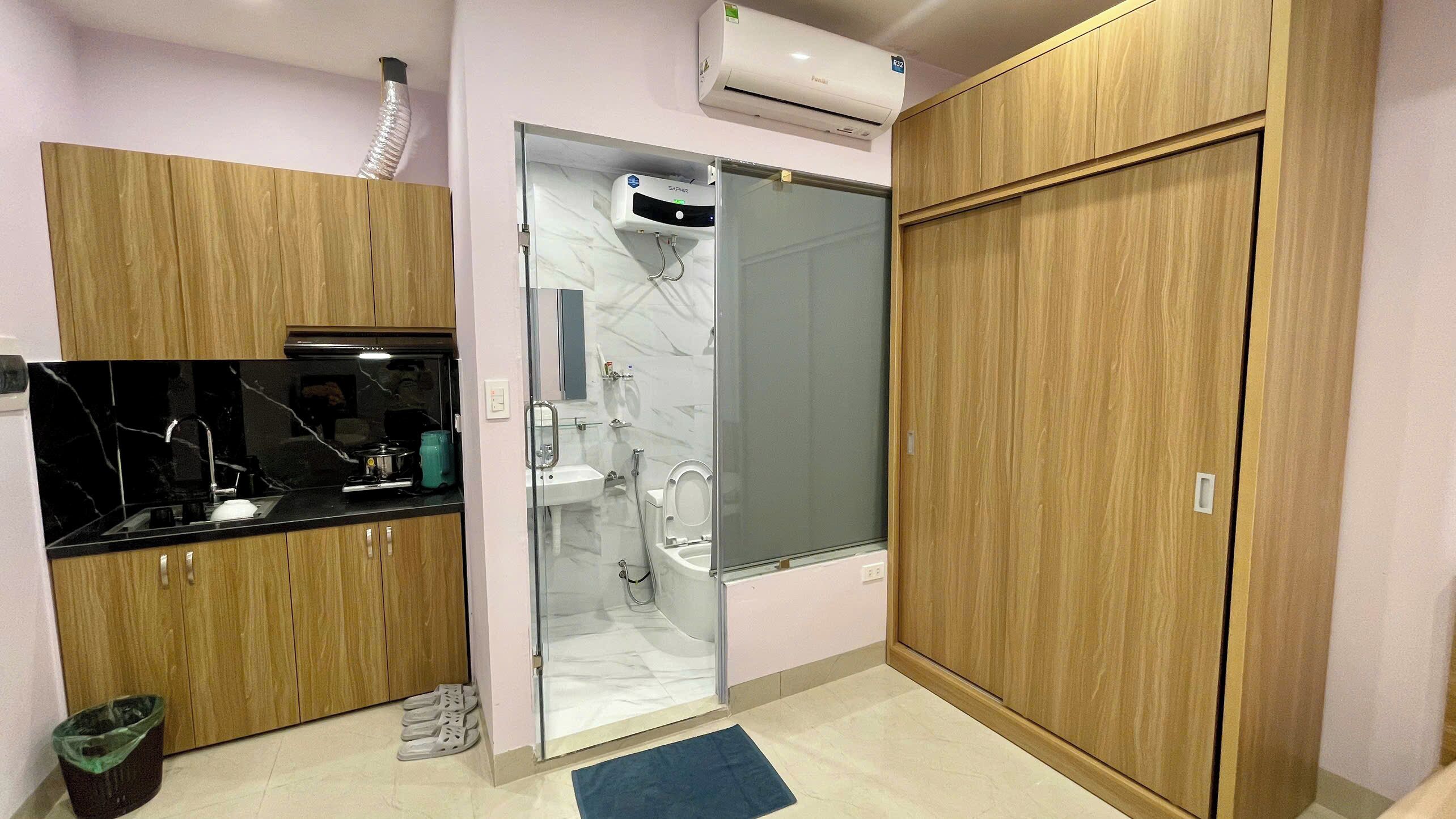 Une petite salle de bain comprenant une douche, des toilettes et un lavabo. On y trouve un meuble en bois avec un plan de travail noir et une poubelle.