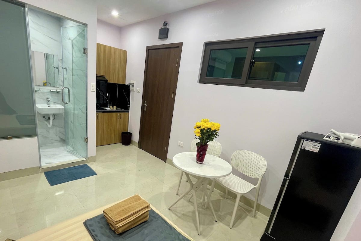 A compact living space with a kitchenette, a dining area with a table and chairs, a small refrigerator, and a bathroom with a glass shower enclosure.