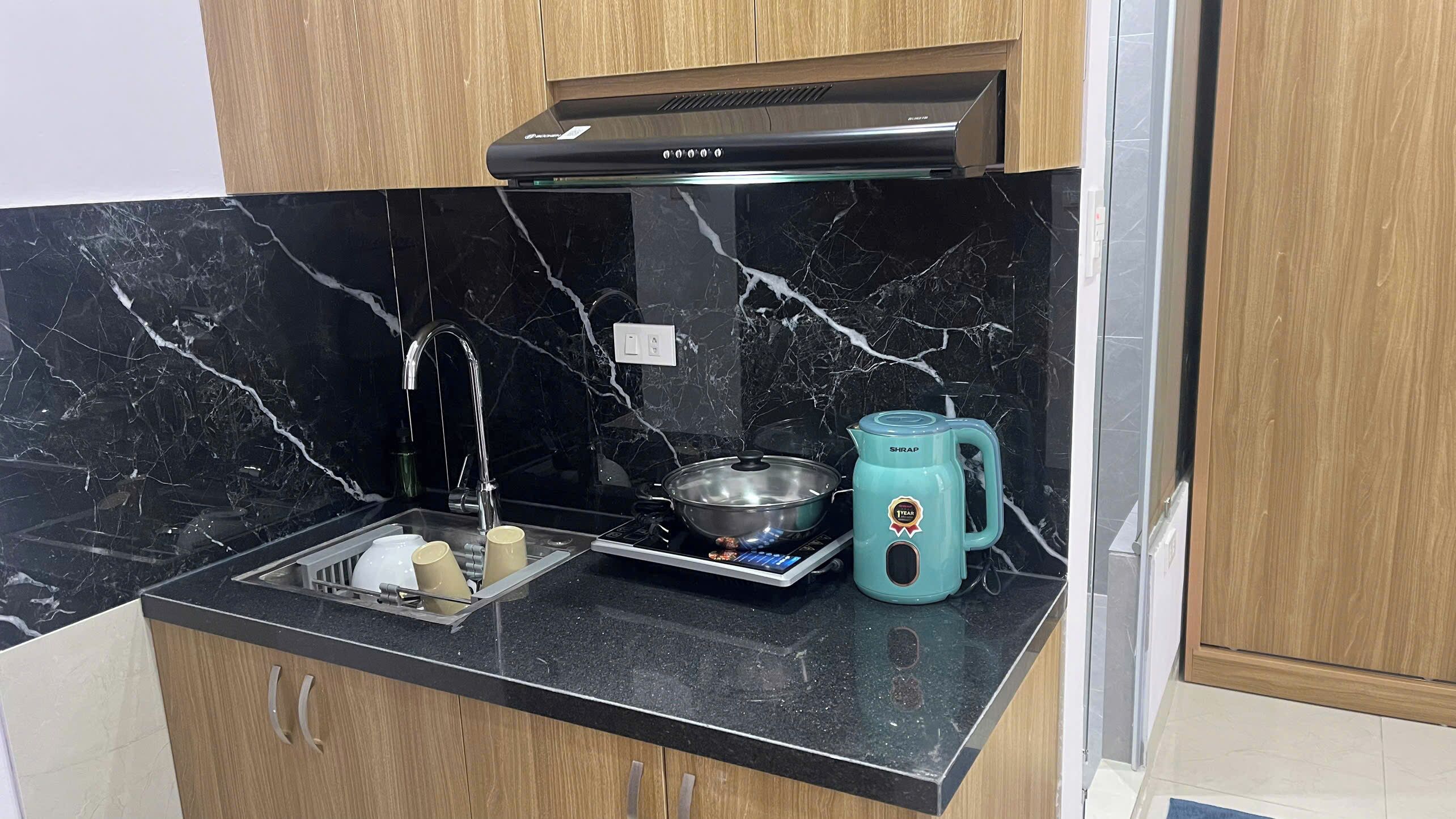 Una cocina con encimera de mármol negro, pileta de acero inoxidable, un hervidor y una olla sobre la hornalla.