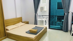 Un dormitorio con una cama de madera, una mesita de noche, una ventana con cortinas y un balcón con barandilla.